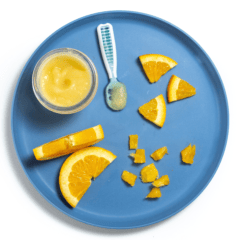 Blue baby plate with different ways to serve oranges to your baby on a white countertop.