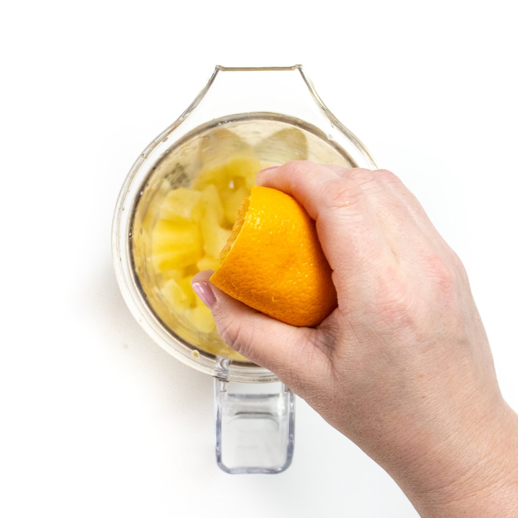 Hand squeezing an orange into a blender with steamed apple chunks.