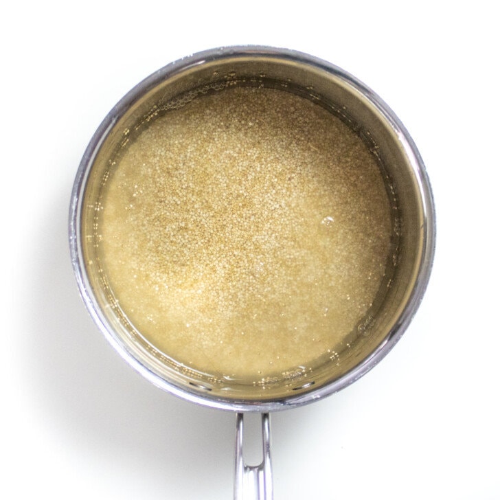 A silver sauce, pan with water and dry quinoa, ready to be cooked sitting on a white counter.