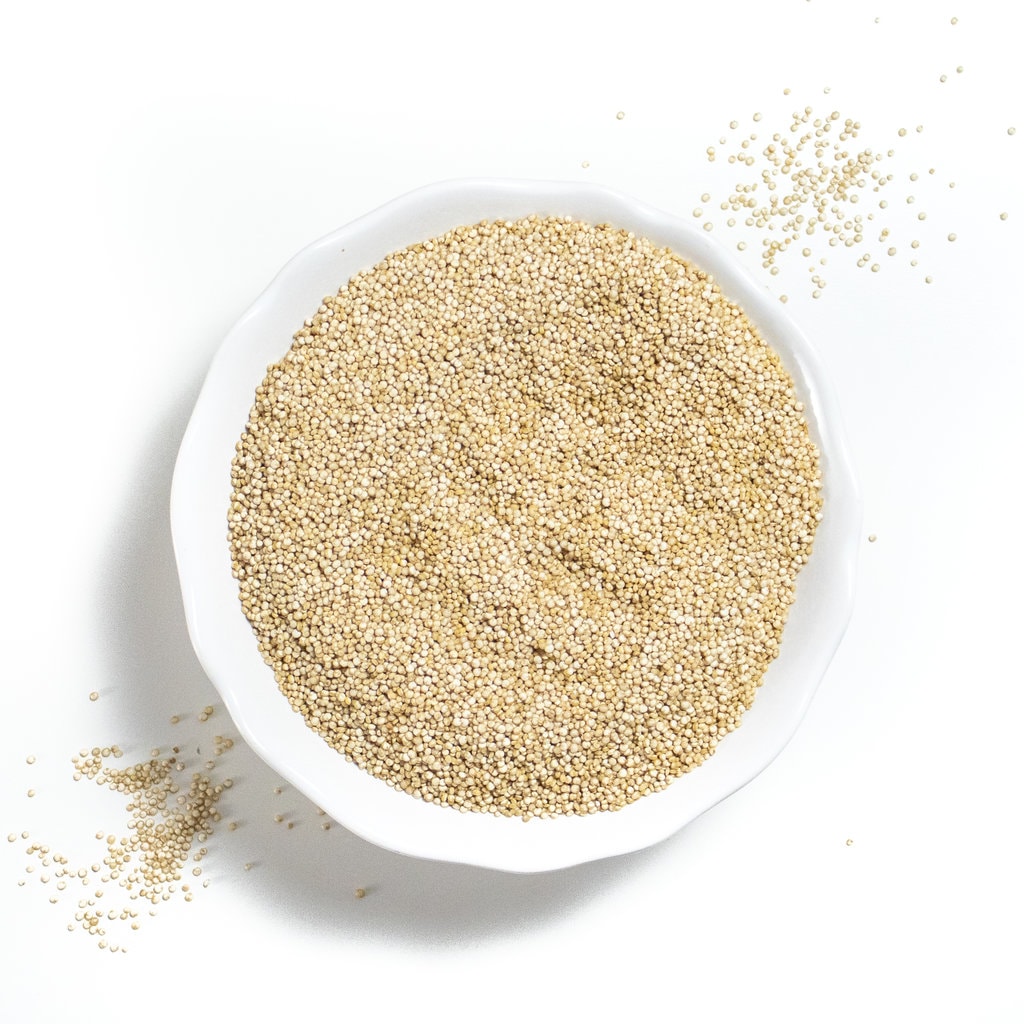 A white bowl with dried quinoa, spilling out of it onto a white countertop.