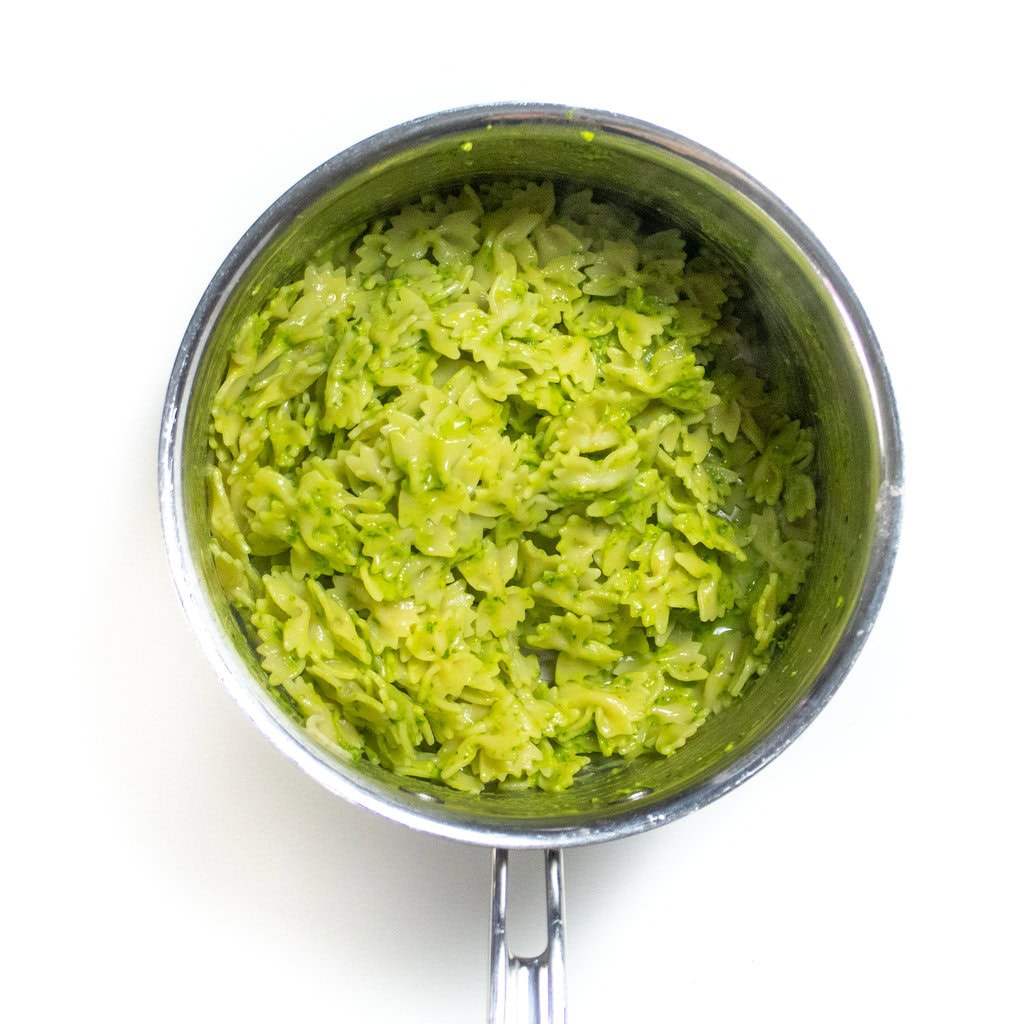 A silvers size pan with bowtie pasta mixed with a creamy green avocado, spinach pesto.