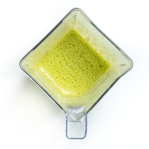 A blender with blended spinach and eggs for scrambled green eggs on a white countertop.
