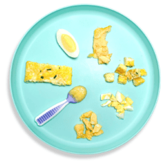Blue baby plate with eggs cooked and cut in different ways to show the variety on how to serve eggs to baby. The plate is sitting on a white countertop.