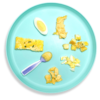 Blue baby plate with eggs cooked and cut in different ways to show the variety on how to serve eggs to baby. The plate is sitting on a white countertop.