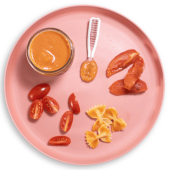 Pink baby plate on white counter showing different ways to serve tomatoes to baby.