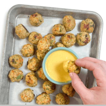 Metal baking tray on my counter, with a hand dipping a meatball into a yellow dip.
