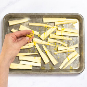 Hands sprinking ginger over sliced parsnips on a baking sheet on my kitchen counter.