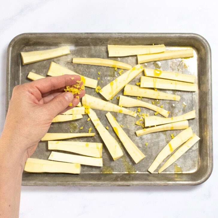 Hands sprinking ginger over sliced parsnips on a baking sheet on my kitchen counter.
