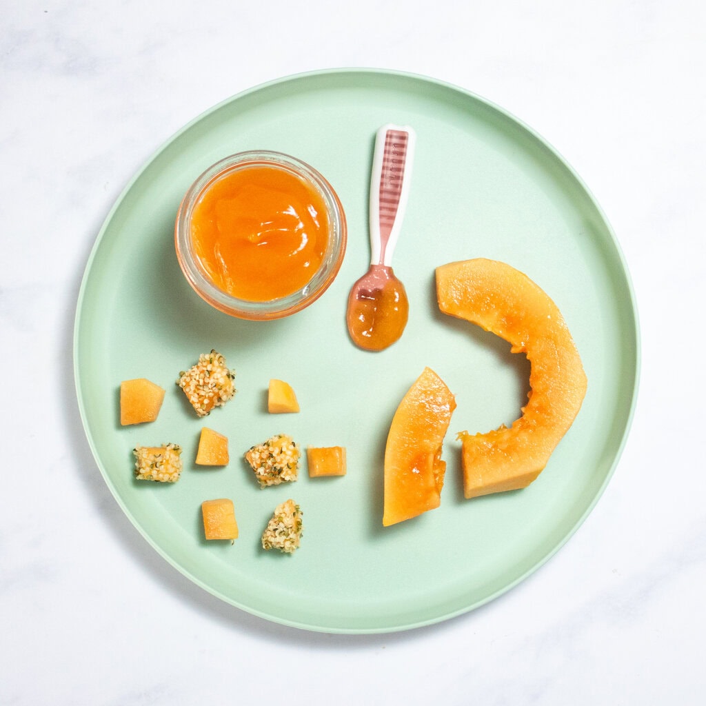 Teal blue kids plate sitting on my white marble counter with papaya cut and pureed in different shapes and textures for baby.