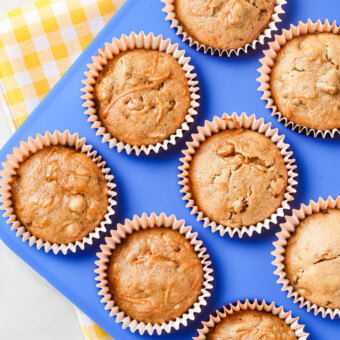 A blue muffin tin with carrot cake muffins inside. Tin is sitting on a yellow and white checkered napkin on my kitchen counter.