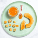 Teal blue kids plate sitting on my white marble counter with papaya cut and pureed in different shapes and textures for baby.