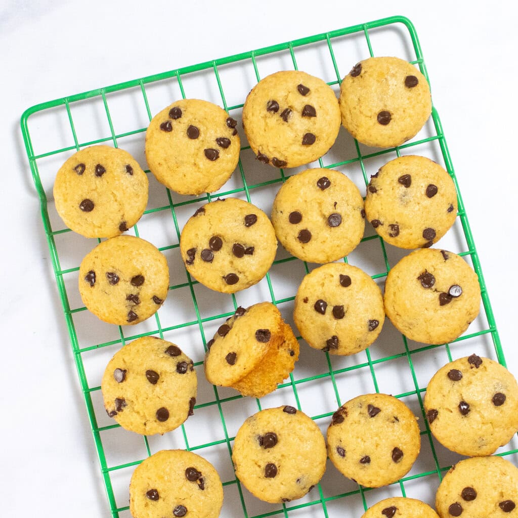 A green wire cooling rack sitting on a white kitchen counter with mini chocolate chip muffins ontop. 