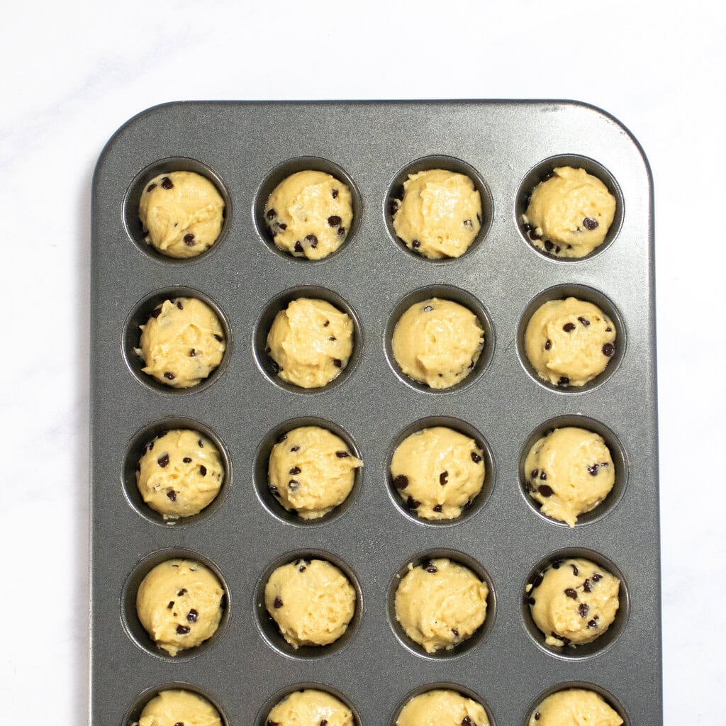 Mini muffin tin sitting on my counter with equal amounts of chocolate chip muffin batter in each section. 