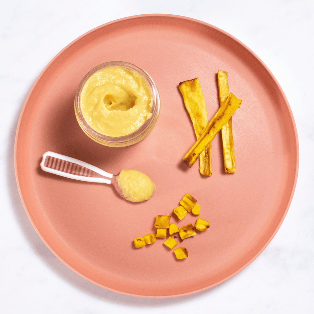 Pink baby plate on a white marble counter with different ways to serve parsnips to your baby - puree, strips for baby-led weaning and chopped for finger foods.