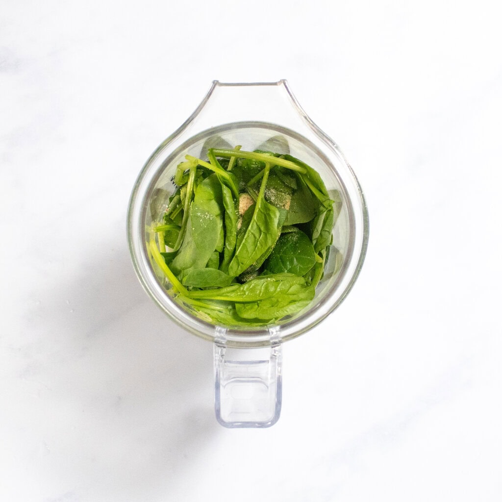 Small blender on my white marble kitchen counter with the spinach, milk and spices in it.