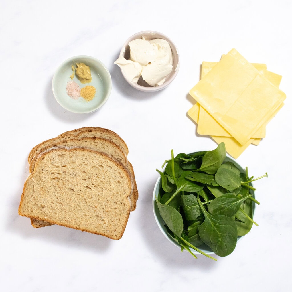 Ingredients for spinach grilled cheese on the counter - bread, spinach, cream cheese, sliced cheese and spices.