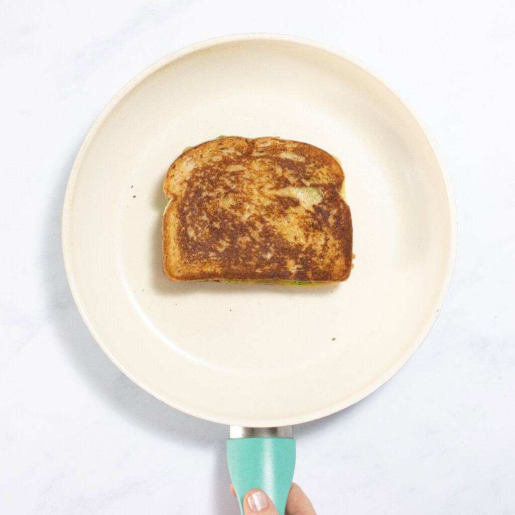 A white skillet over my kitchen counter with a golden brown grilled cheese on it.