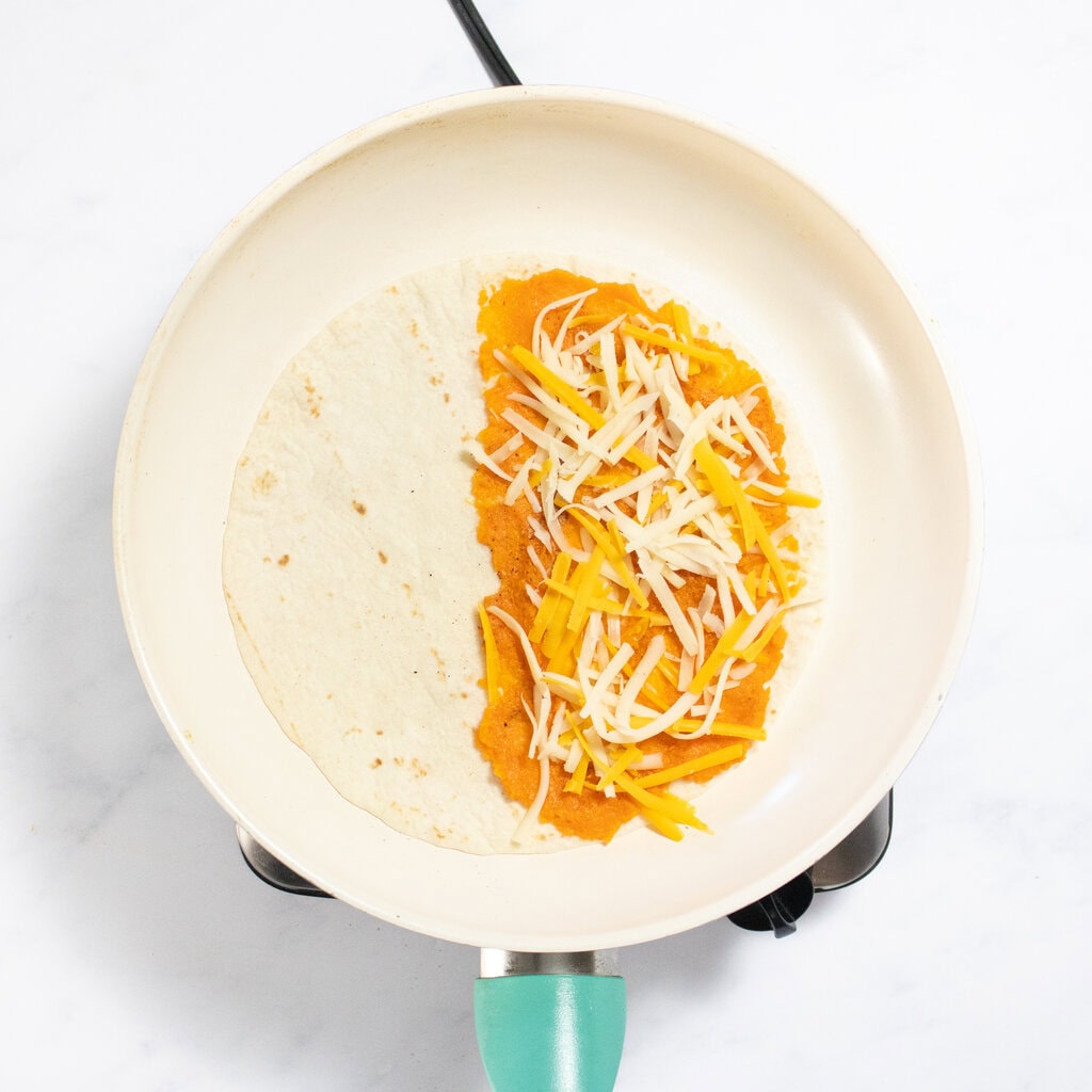 Process shot of how to layer a sweet potato quesadilla on a skillet.