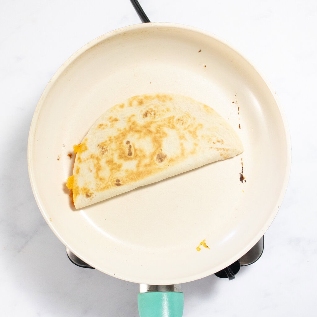 Half a quesadilla getting cooked in a white skillet.