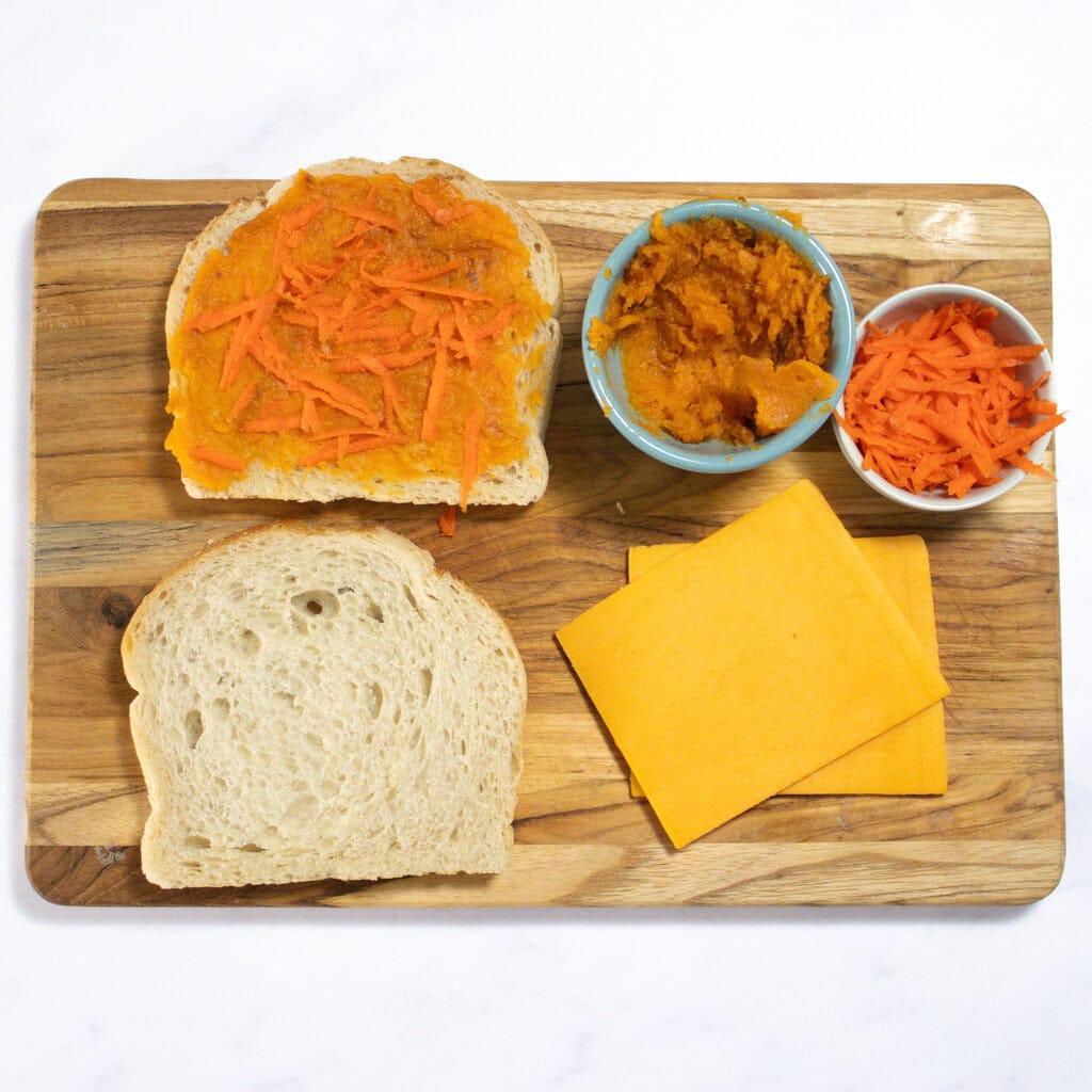 A wooden cutting board in my kitchen showing how to layer the sweet potato and carrots onto the bread.