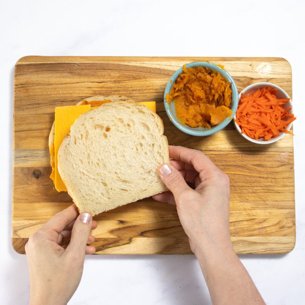 A wooden cutting board with my hands showing how to build a veggie grilled cheese.