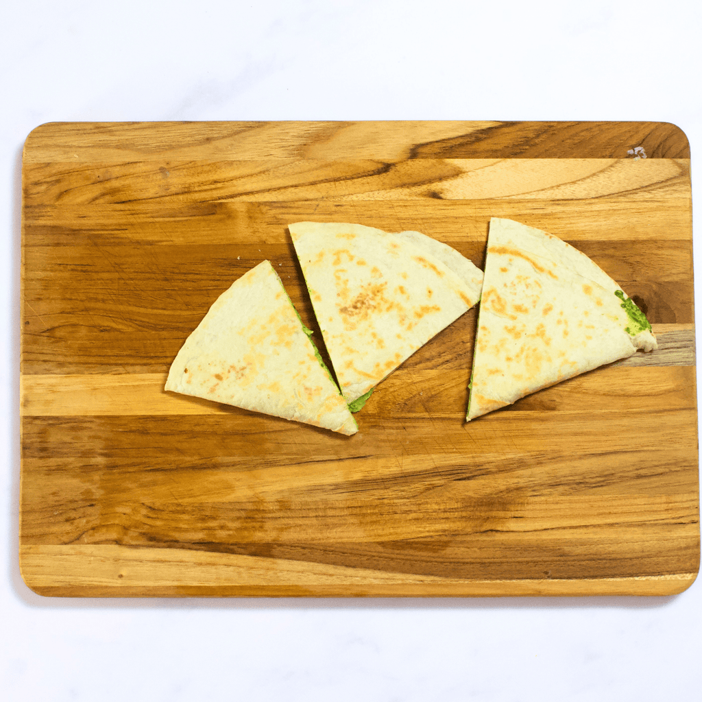 Cutting board with three wedges of spinach quesadillas on it.